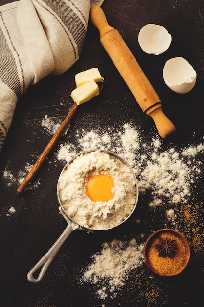 暗い古い素朴なテーブルの上に小麦粉、卵、砂糖、バター、シナモン、アニススター、キッチンツールの材料で表面を焼く。セレクティブフォーカス。トーン画像。上面図。