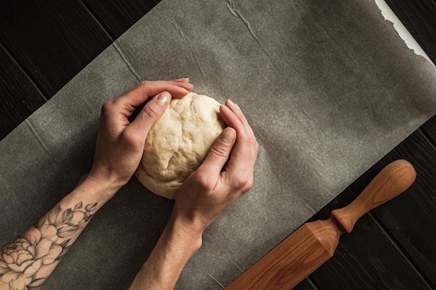 写真 甘いカッテージチーズの編みこみのパンをレーズンとジャムで焼きます。羊皮紙の上に、麺棒で生地を持っている女性の手。オーバーヘッドショット。