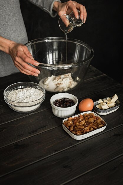 Baking sweet cottage cheese braided bread with raisins and jam. Ingredients on a wooden table. Adding olive oil into a big bowl. Lifestyle image.