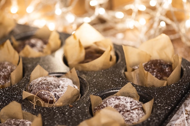 Baking tin with a tasty chocolate muffins on the wooden table