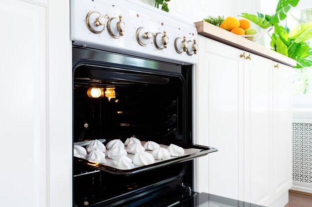 Baking tray with sweet meringues in the oven on kitchen.