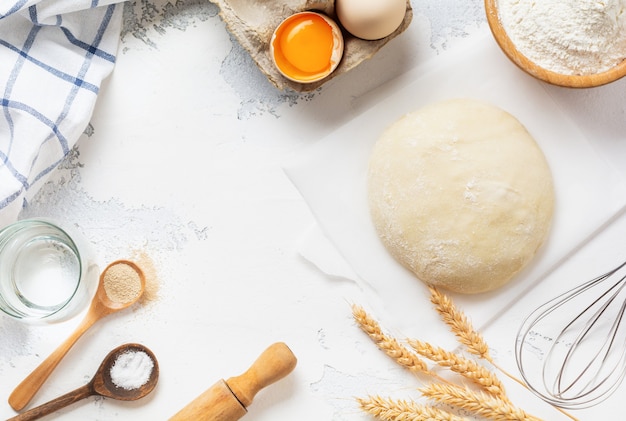 Baking wall with dough and ingredients for the preparation of pasta or pancakes, eggs, flour, water and salt on white rustic old table. Top view.