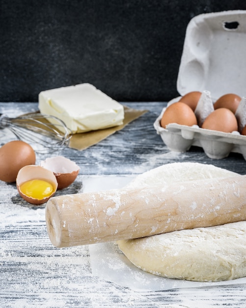 Bakken deeg voor pizza met deegroller op houten tafel. Bakken ingrediënten van eieren, meel, boter.