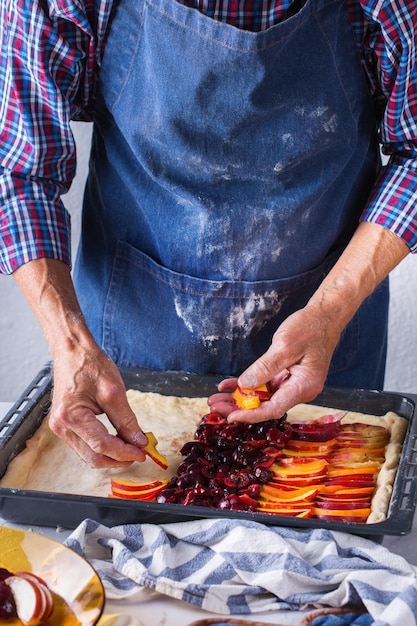 Bakken eten thuis gezonde voeding en lifestyle concept Senior bakker man koken kneden van vers deeg met handen rollen met pin verspreiding van de vulling op de taart op een keukentafel met bloem