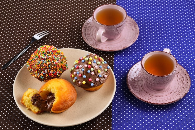 Bakken met thee en chocolade op tafel. Twee kopjes thee met cupcakes en chocolade met een veelkleurige poeder op tafel.