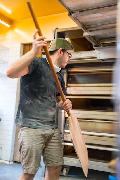 Foto bakker van de bakkerij in de werkplaats ambachtelijke werkplaats bakken het verwijderen van de broden uit de oven met de schop