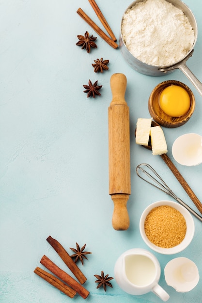 Bakoppervlak met ingrediënten meel, eieren, suiker, boter, kaneel, anijs ster en keukengerei op blauwe rustieke tafel. Selectieve aandacht. Bovenaanzicht.