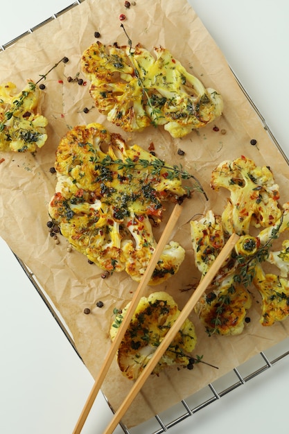 Bakrek met gebakken bloemkool en houten tang op witte achtergrond.