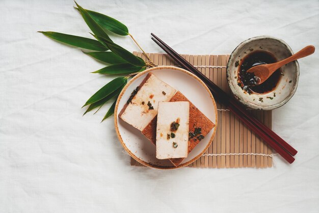 Baksteen van biologische gerookte tofu-kaas met sojasaus en bamboebladeren. plat leggen. bovenaanzicht. veganistisch snackconcept