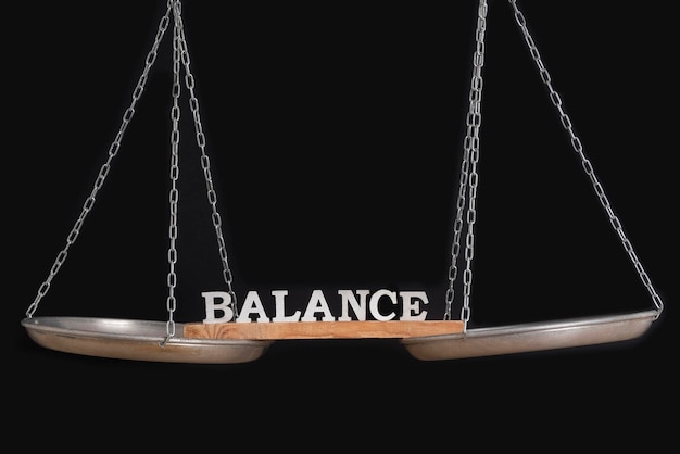 Balance scales on black background close up Word BALANCE on scales on black background