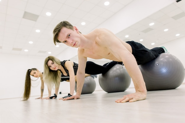 Balance, strength concept. Sporty man and two women do handstand with legs on fit ball. People in sportswear training on fitball in gym. Sport, fitness training