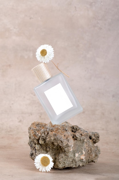 Balanced bottle of perfume with white labels on stone podium on beige terracotta background with dry flower