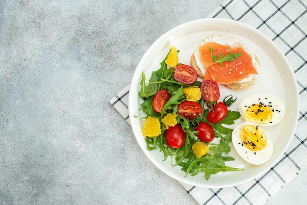 Photo balanced breakfast with fish sandwich boiled egg and vegetables on grey background