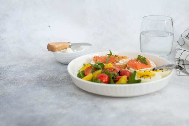 Balanced breakfast with fish sandwich boiled egg and vegetables on grey background