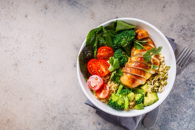 Photo balanced food concept. chicken, broccoli and quinoa salad in white bowl, gray background, top view.