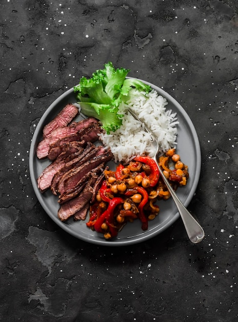 균형 잡힌 건강한 점심 쇠고기 스테이크 쌀과 구운 가지 고추 병아리콩 스튜는 어두운 배경의 꼭대기에서 볼 수 있습니다.