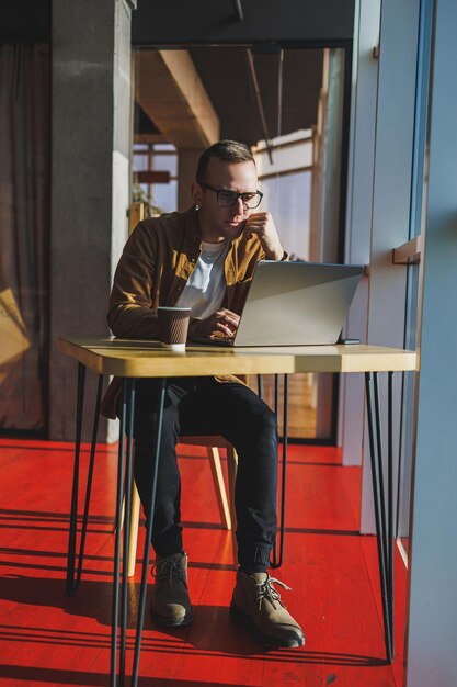 A balanced man in glasses and casual clothes works on a laptop from a cozy workspace A successful freelancer works remotely