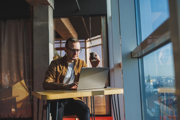 A balanced man in glasses and casual clothes works on a laptop from a cozy workspace A successful freelancer works remotely