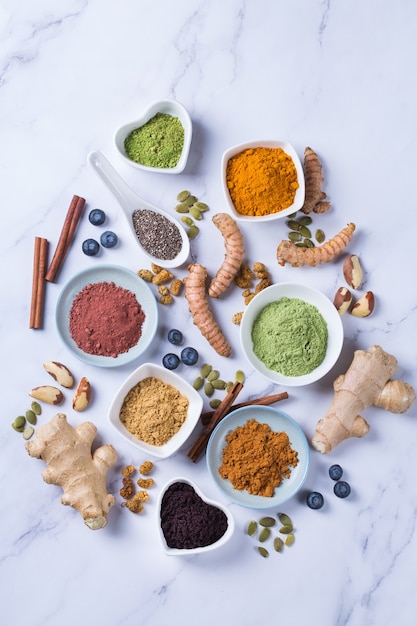 Balanced nutrition concept for clean eating antioxidant detox diet. Assortment of superfood powder - acai, turmeric, wheat, ginger, cinnamon, matcha. Flat lay marble background