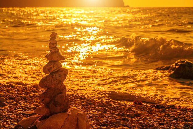 Balanced pebble pyramid on the beach on a sunset time sea waves and foam on the background selective