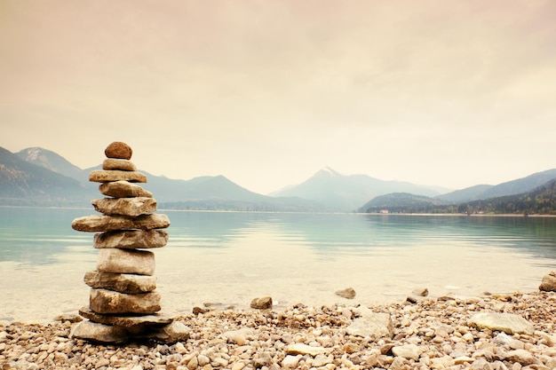 Photo balanced stone pyramide on shore of blue alpine lake  blue mountains in water level mirror