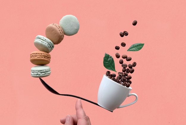 Photo balancing cup of coffee and macarons on a spoon on coral wall