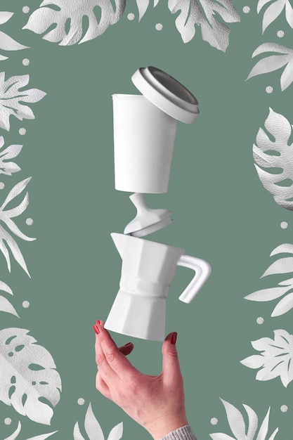Балансировка ноль отходов кофе пирамиды в женских руках на фоне зеленого salbei. Керамическая кофеварка эспрессо и экологически чистая многоразовая бамбуковая кофейная кружка. Кофе в зернах и экзотическая бумага листья вокруг.