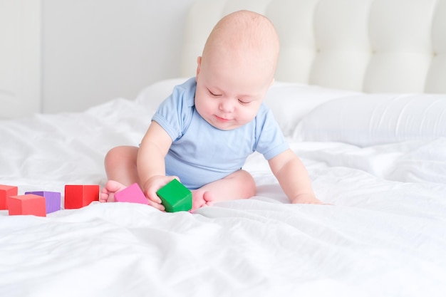 bald baby boy 3 months in blue bodysuit playing with children wooden cubes toys on bed