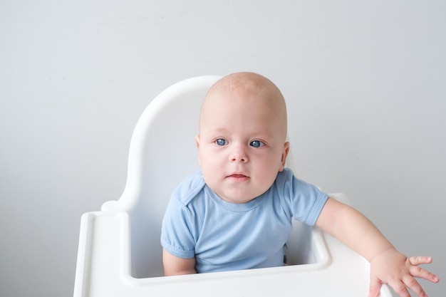 лысый мальчик 3 месяца сидит в детском кресле на белом фоне