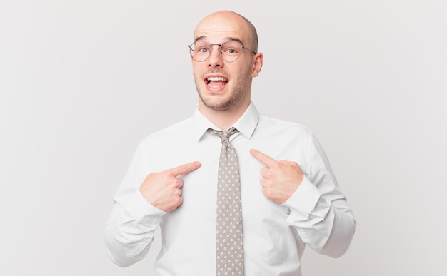 Bald businessman feeling happy, surprised and proud, pointing to self with an excited, amazed look