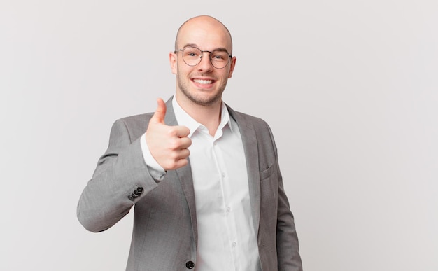 Bald businessman feeling proud, carefree, confident and happy, smiling positively with thumbs up