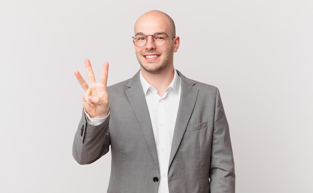 Bald businessman smiling and looking friendly, showing number three or third with hand forward, counting down