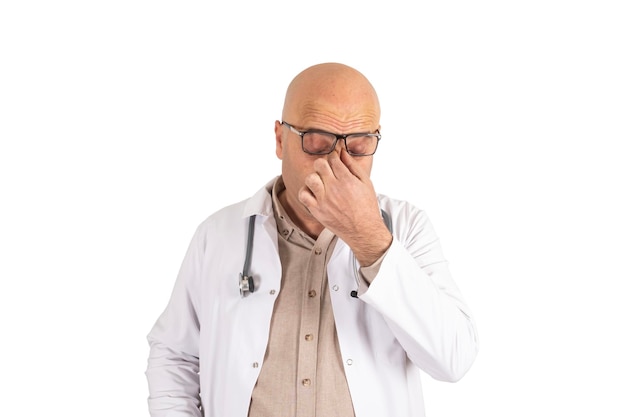 A bald doctor with a stethoscope and glasses holds his nose in pain Stressed physician