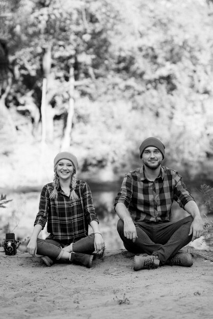 Bald guy with a beard and a blonde girl in bright hats on the background of the river are taking pictures with an old camera