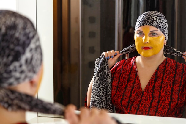 Photo a bald jewish woman on her face with a cosmetic mask puts on a traditional headdress