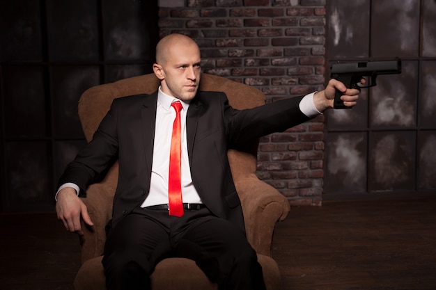 Bald killer in suit and red tie aims a pistol