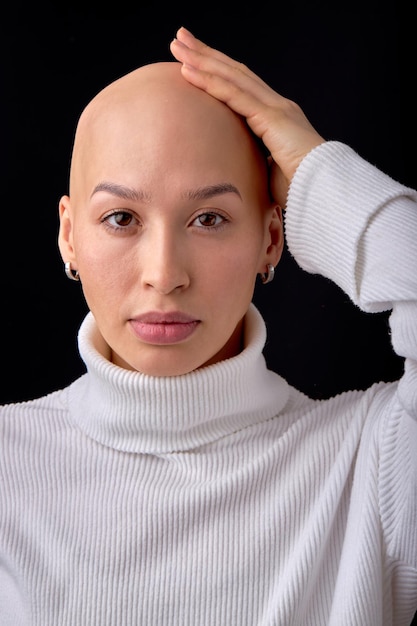 Bald lady on black studio background, looks at camera, confident. she feels awkward due to falling hair. concept of oncology and effects of chemotherapy. portrait copy space. people, healthcare