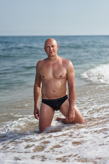 Uomo calvo sulla spiaggia in riva al mare in vacanza