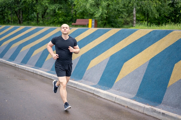 bald man in black clothes running in the park in summer, close-up