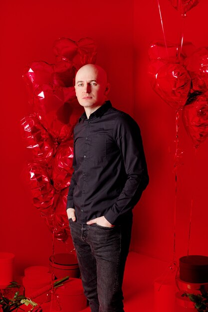 Bald man in a black shirt stands with heart-shaped balloons 