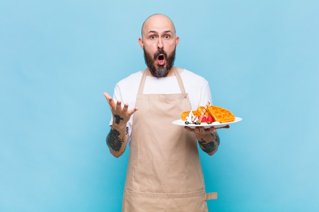 Bald man feeling extremely shocked and surprised, anxious and panicking, with a stressed and horrified look