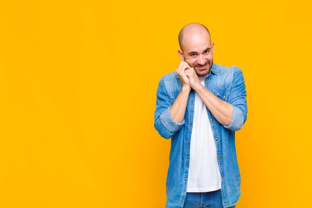 Bald man feeling in love and looking cute, adorable and happy, smiling romantically with hands next to face