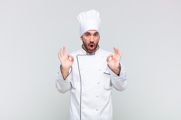 Bald man feeling shocked, amazed and surprised, showing approval making okay sign with both hands