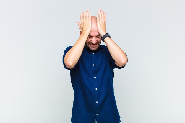 Bald man feeling stressed and anxious, depressed and frustrated with a headache, raising both hands to head