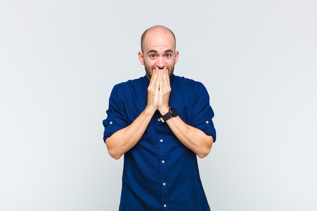 Bald man happy and excited, surprised and amazed covering mouth with hands, giggling with a cute expression