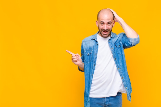 Bald man laughing, looking happy, positive and surprised, realizing a great idea pointing to lateral copy space