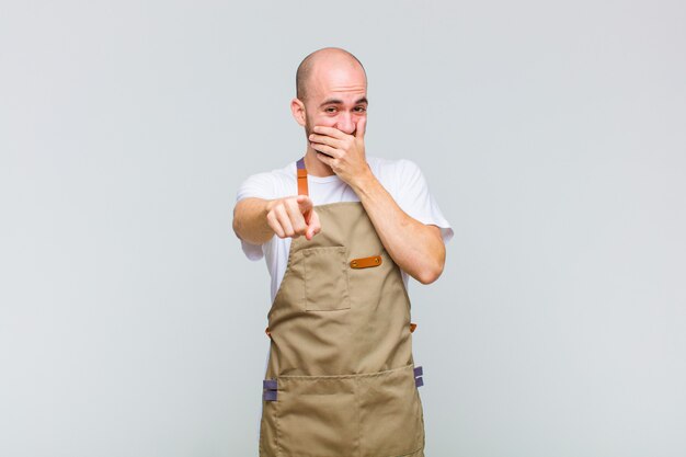 Bald man laughing at you, pointing to front and making fun of or mocking you