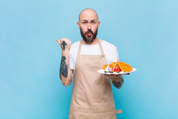 Bald man looking astonished in disbelief, pointing at object on the side