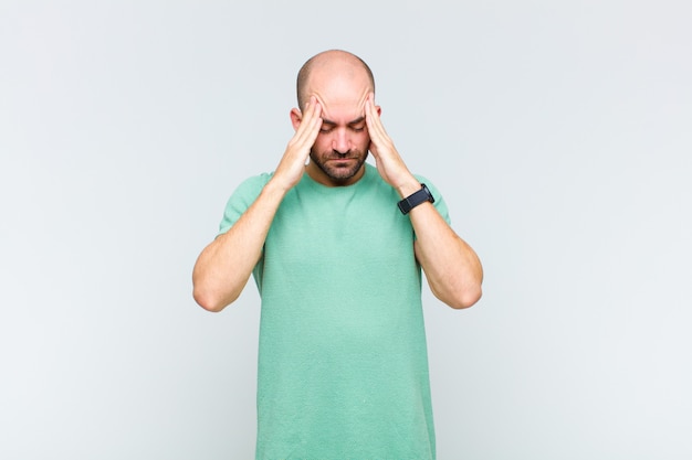 Bald man looking concentrated, thoughtful and inspired, brainstorming and imagining with hands on forehead