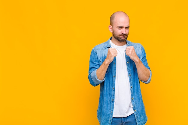 Bald man looking confident, angry, strong and aggressive, with fists ready to fight in boxing position